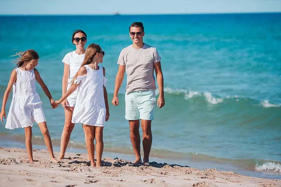 A young family wearing white enjoying a sandy beach.